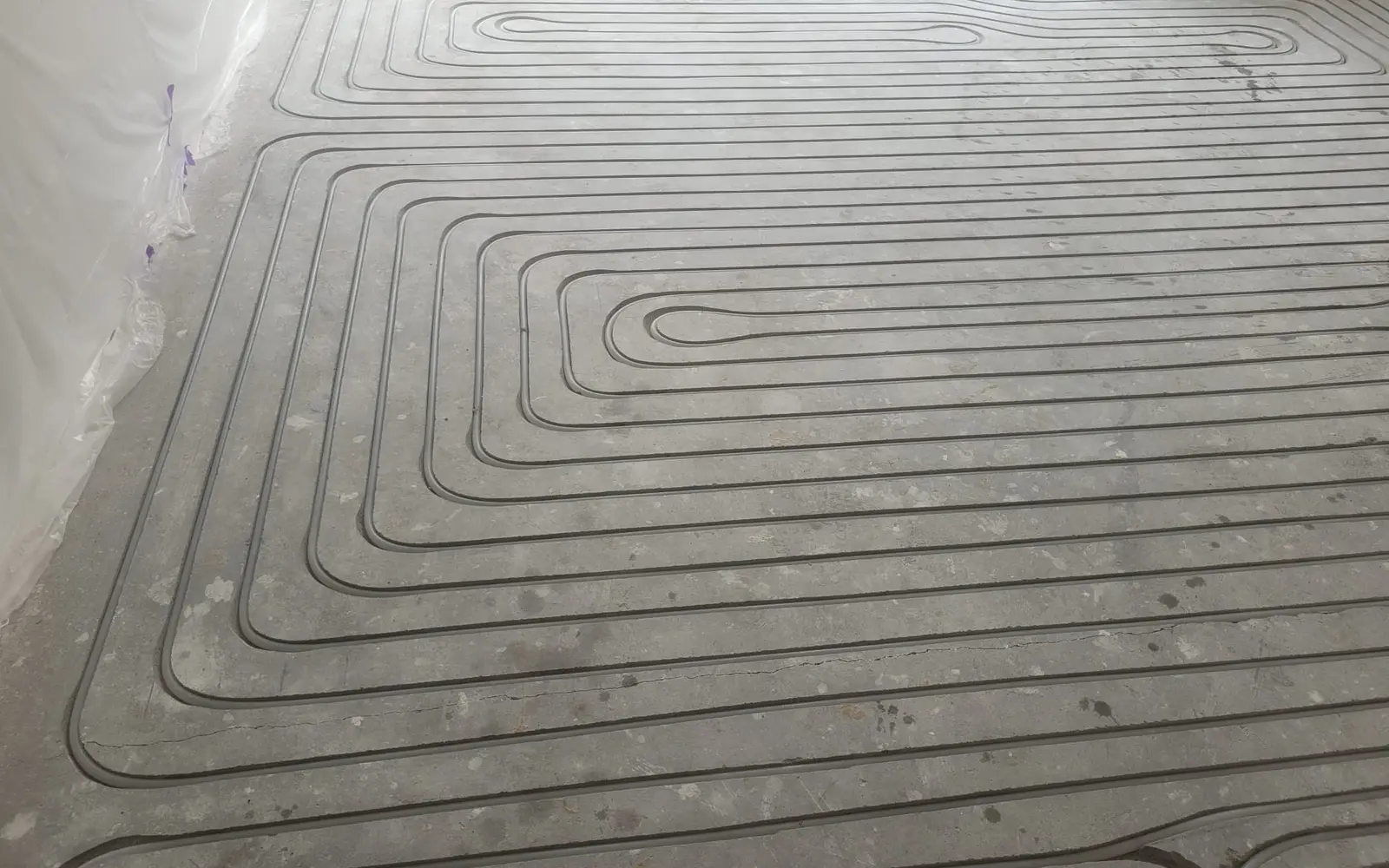 Ingefreesde sleuven met vloerverwarmingsbuizen in een rond patroon in een betonnen dekvloer, met afgeschermde wanden